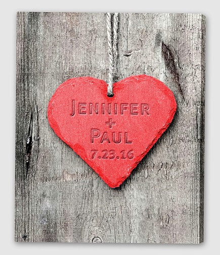 Canvas print with red embossed heart on couples names and date stands out on woodgrain background in gray scale. 